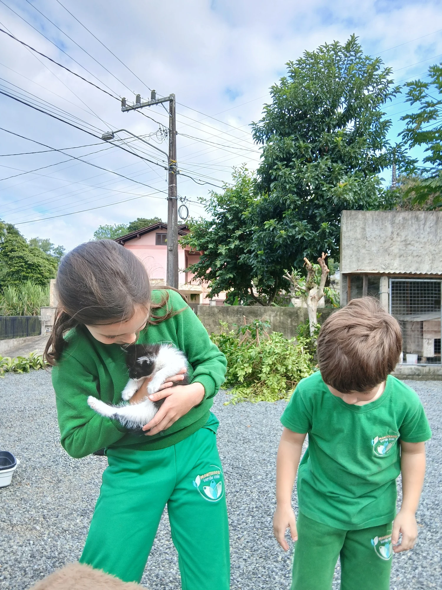 Duas crianças ao ar livre, uma delas acolhendo um gatinho nos braços